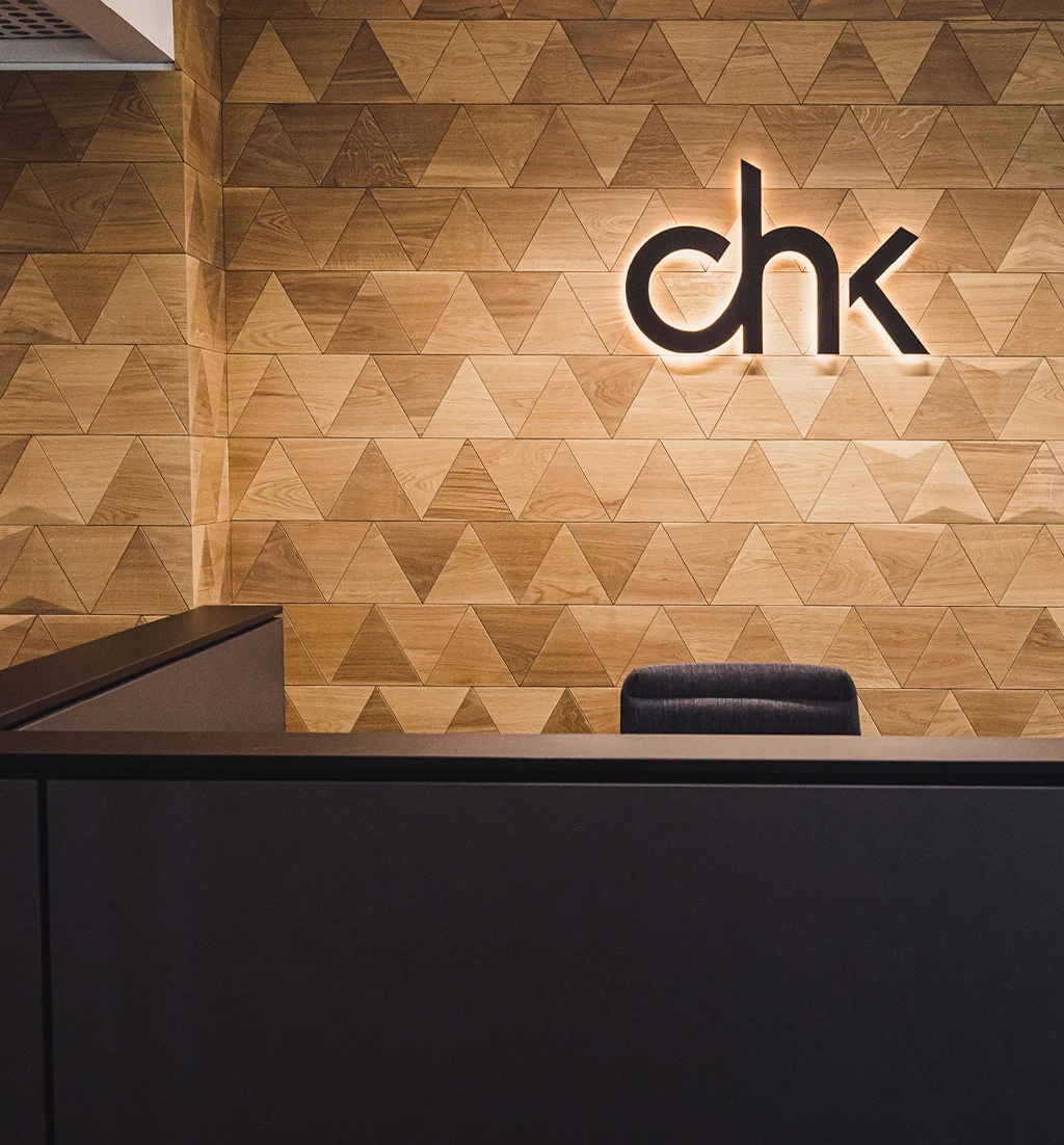 Wandgestaltung im Büro-Empfangsbereich mit dreieckigen Holzpaneelen aus Eiche und einem hinterleuchteten Logo.