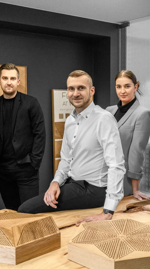 A team of three interior designers presenting unique perforated oak wood panels on a solid wood table.