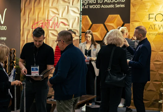 Team präsentiert 3D-Akustikpaneele aus Eiche und Wandkollektionen auf einer Fachmesse für Inneneinrichtung.