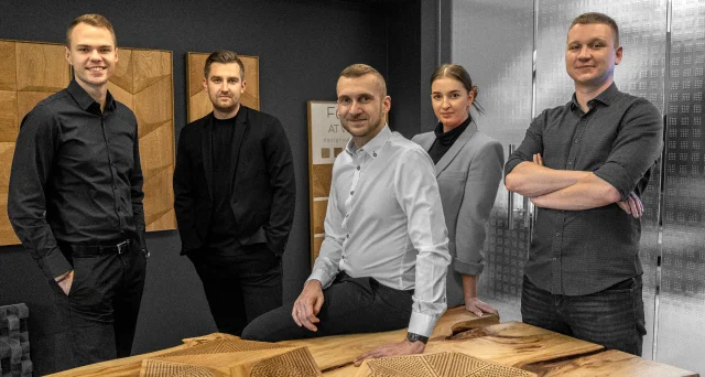 Zespół projektowy w showroomie producenta dębowych paneli 3D, prezentujący nowoczesne rozwiązania ścienne i meble z litego drewna.